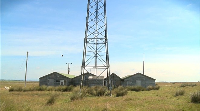 Remains of Haverah Park cosmic ray observatory near Leeds. Some wooden huts and a tall gantry tower.