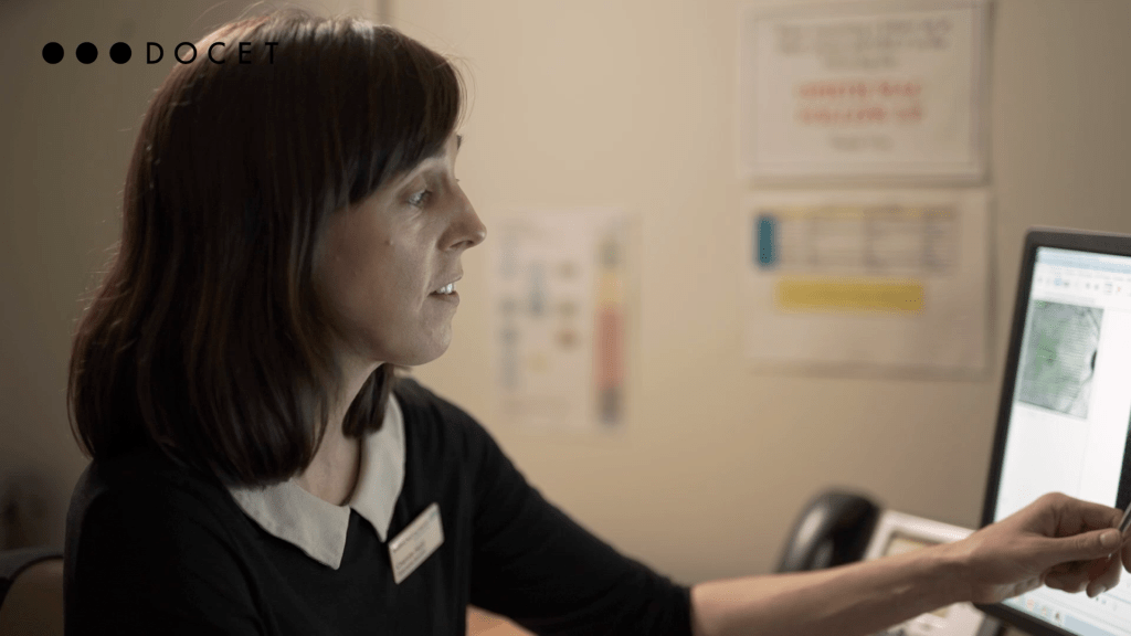 An optometrist points at data displayed on her computer screen
