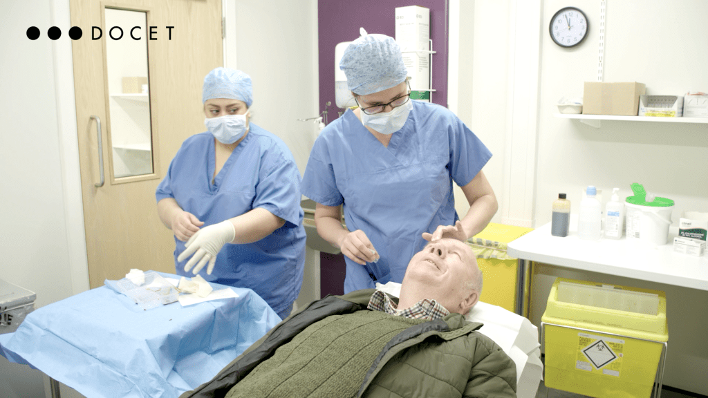 A man is lying down in a hospital surgery room while two medics in blue prepare to treat the patient's eye