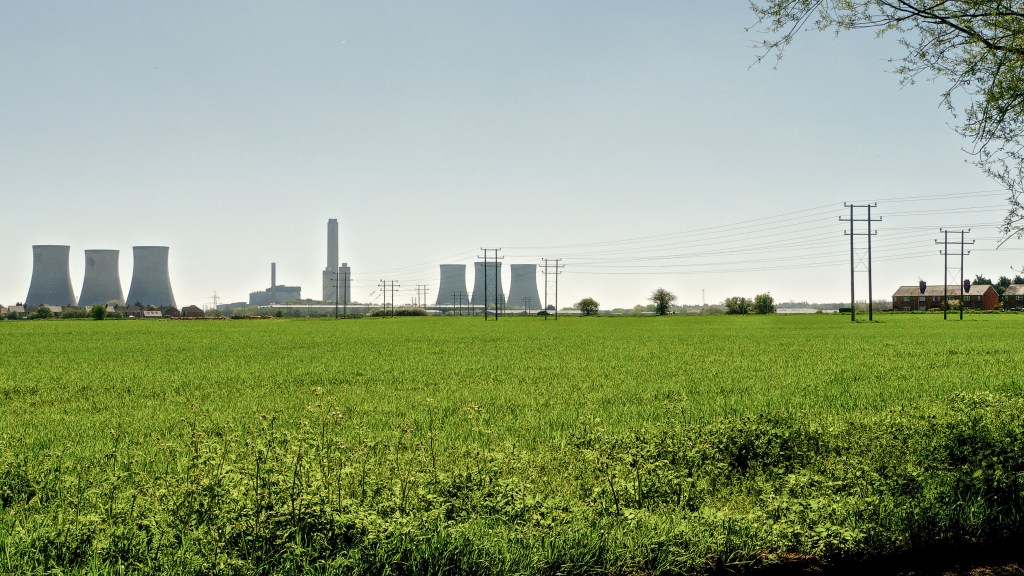 Two sets of cooling towers and the central power station building with green fields in foreground