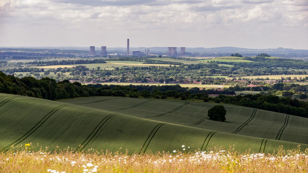 View from a high hill, cooling towers in distance, large oak tree in field in foreground