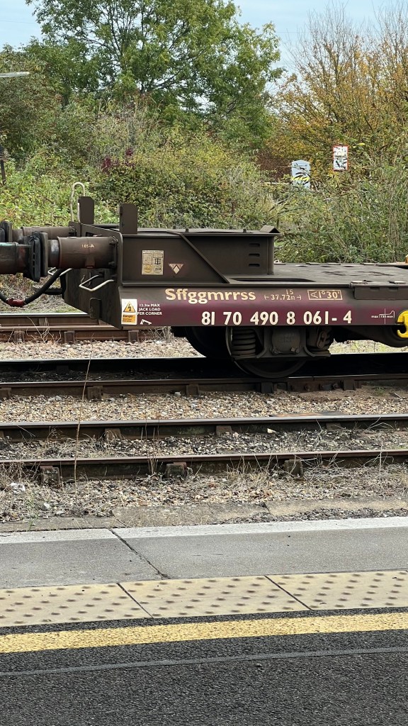 Side on view of the left end of a flat train wagon with letters and numbers painted on
